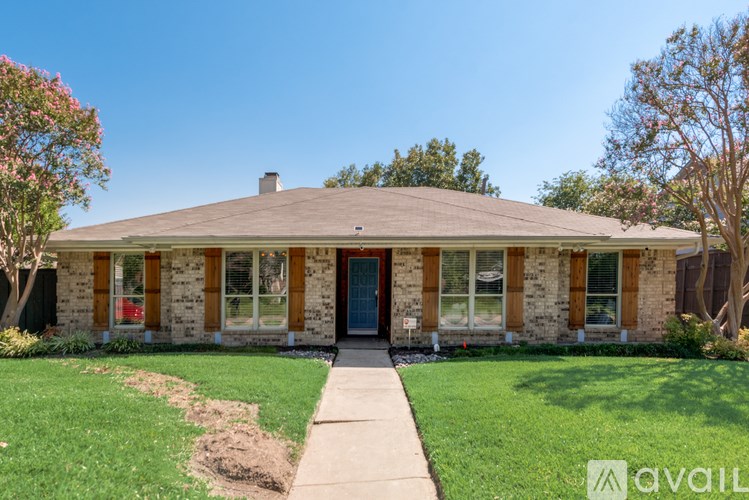 A house with a brown roof and a blue door is surrounded by green grass and trees.