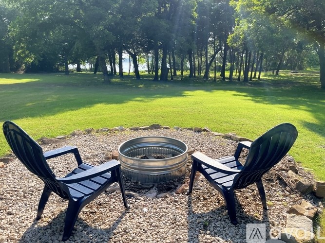 Two black chairs are placed on a gravel area with a metal bowl between them.
