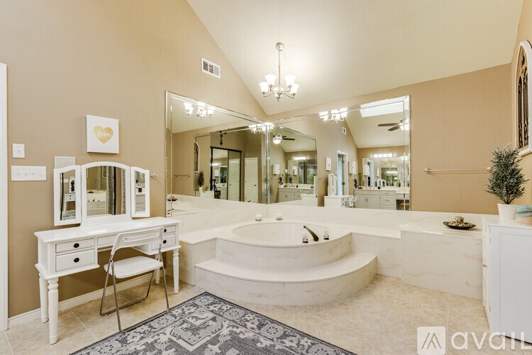 A bathroom with a large mirror, a bathtub, and a vanity with a chair.