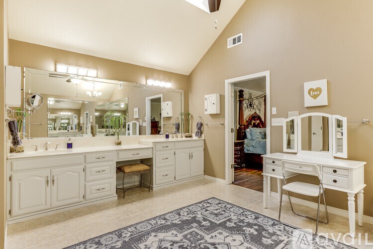 A large white vanity with a mirrored back wall and a white desk with a chair.