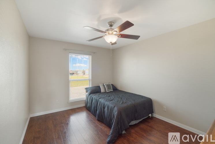 A bedroom with a bed, ceiling fan, and a window overlooking a lawn.