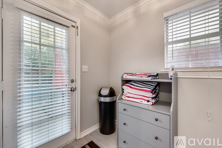 A room with a white door, a grey shelf with folded towels, and a black trash can.