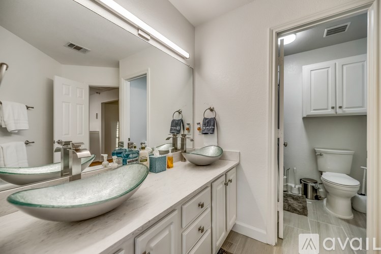 A bathroom with a glass sink and a toilet in the background.