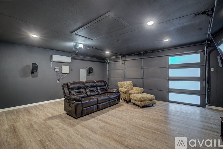 A spacious room with a black leather couch and matching ottoman, a wooden floor, and a wall-mounted air conditioner unit.