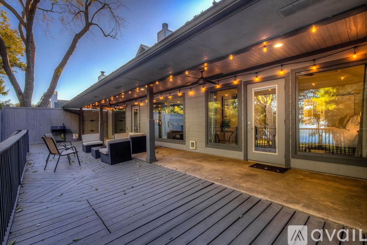 A wooden deck with a table and chairs is lit up with string lights.