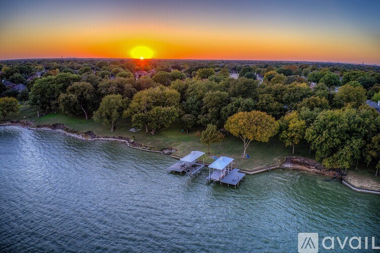 A sunset view of a tree-lined coastline with a dock and a house.