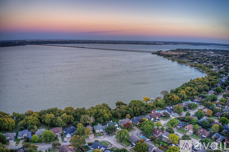 A beautiful aerial view of a residential area with houses and trees, overlooking a large body of water during sunset.