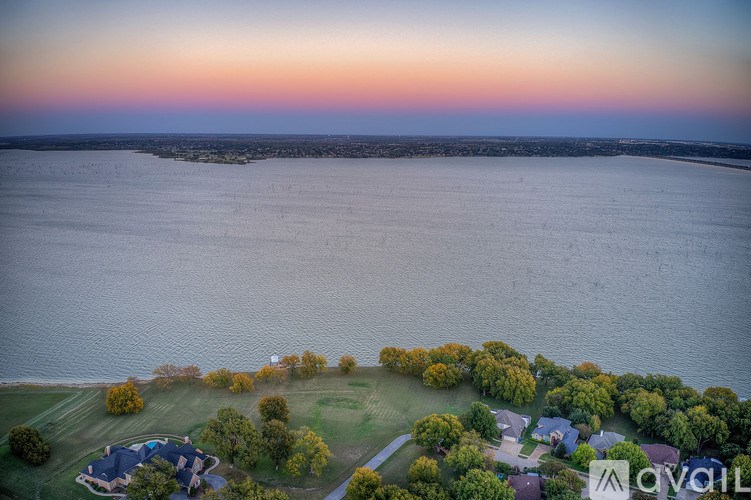 An aerial view of a house surrounded by trees and a body of water at sunset.