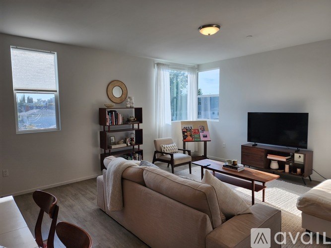 A living room with a beige couch, a wooden coffee table, a flat screen TV, and a bookshelf with various items.