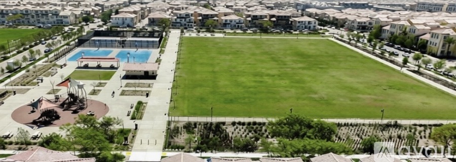 A large grassy field is surrounded by a pool and a fence.