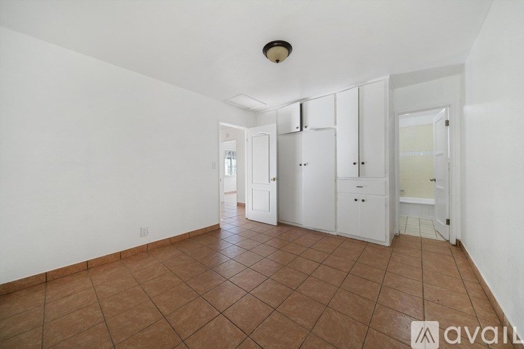A room with white walls and brown tile flooring with a white cabinet and a white door.