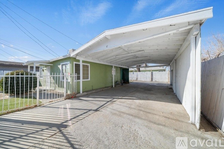 A covered outdoor area with a white roof and a green house in the background.