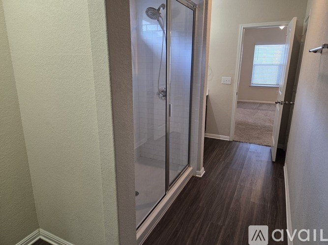 A bathroom with a glass shower door and wooden flooring.