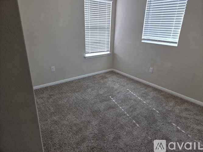 A room with carpeted floor and two windows with blinds.