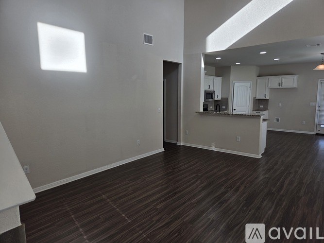 A room with wooden flooring and a kitchen area in the background.