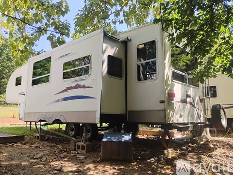 A white RV with a blue stripe and a logo is parked in a wooded area.