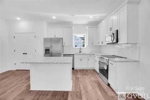 A modern kitchen with white cabinets and a wooden floor.