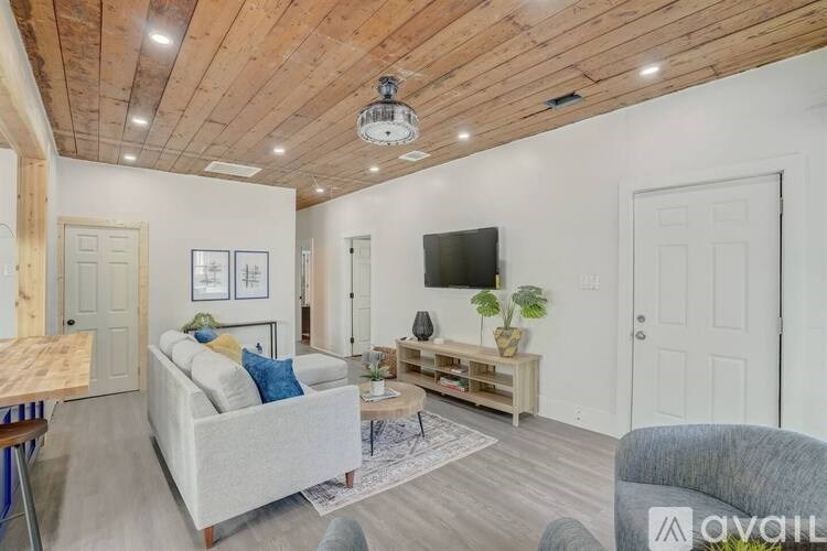 A living room with a grey couch, a wooden coffee table, and a TV on the wall.