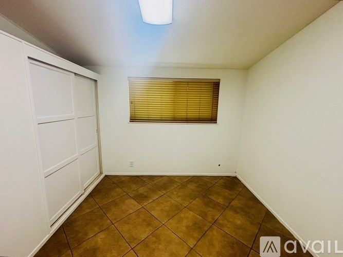 A room with a brown tile floor and a window with blinds.