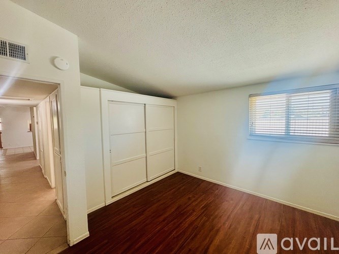 A room with wooden floors and white walls, with a window on the right side.