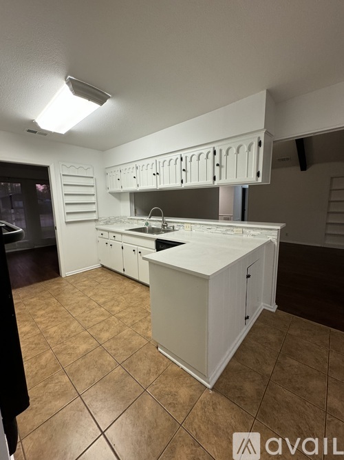 A kitchen with white cabinets and brown tiled flooring.