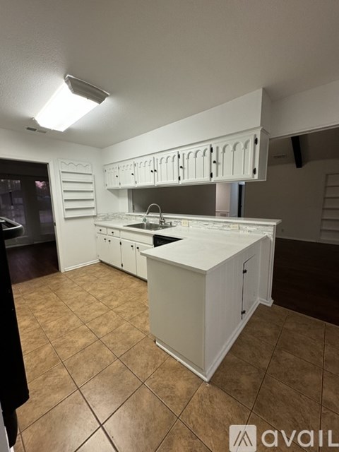 A kitchen with white cabinets and brown tiled flooring.