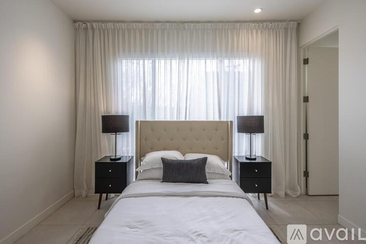 A bedroom with a large bed, two nightstands, and a window with curtains.