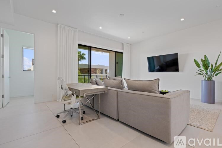 A modern living room with a grey sofa, a white chair, and a flat-screen TV mounted on the wall.