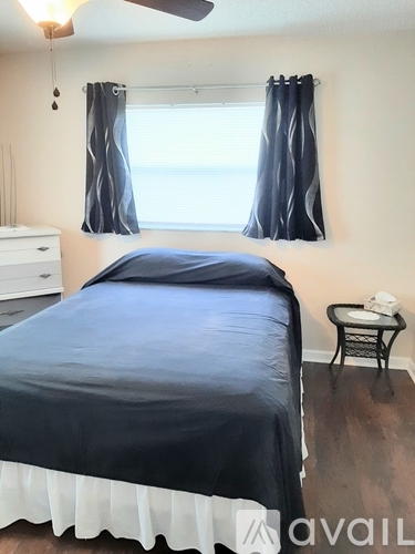 A bedroom with a bed, a small table, and a window with curtains.