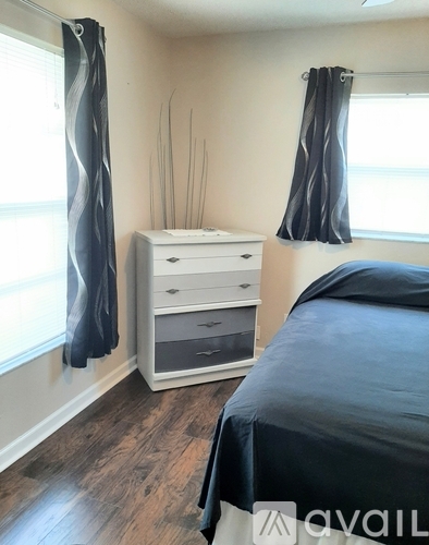 A bedroom with a bed, dresser, and window with curtains.