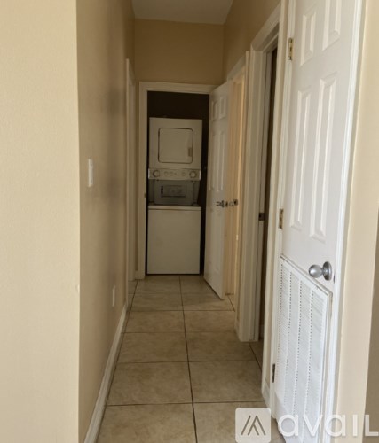 A hallway with a white door on the right and a white cabinet with a microwave and oven in the middle.