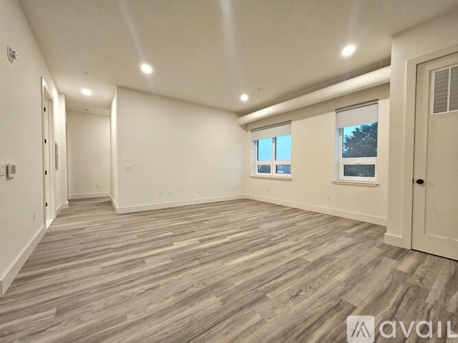 A spacious room with wooden flooring and two windows.