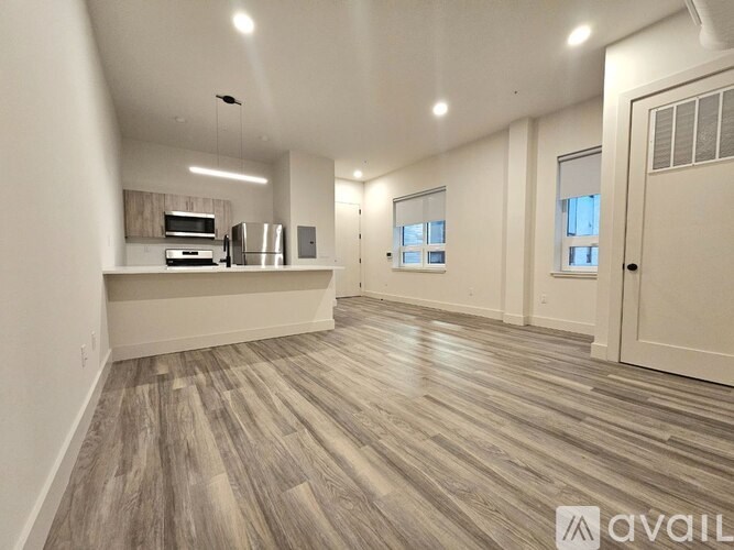 A spacious room with wood flooring and a kitchenette area.