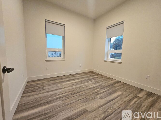 A room with wooden flooring and two windows.