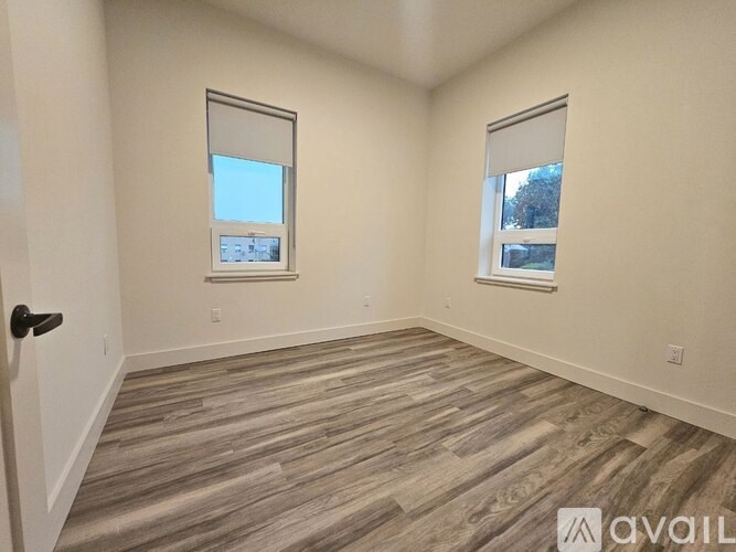 A room with wooden flooring and two windows.