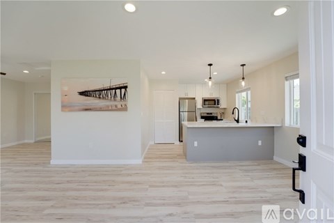 A spacious living room with a large painting on the wall and a kitchen area in the background.