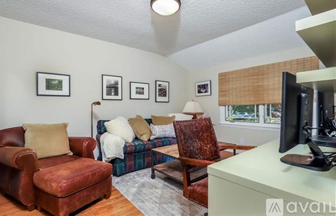 A living room with a red leather chair, a couch with a plaid blanket, a coffee table, and a flat-screen TV.
