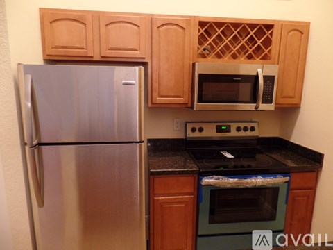 A kitchen with a stainless steel refrigerator, wooden cabinets, and a black countertop with a stove and oven.