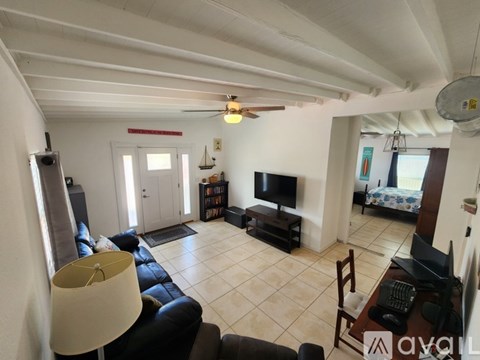 A living room with a black leather couch, a television, and a ceiling fan.