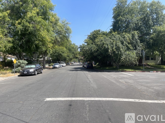 A street with cars parked on the side and trees lining the road.