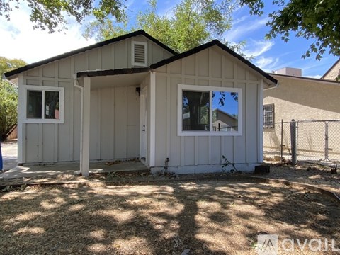 A small white house with a black roof and a fence in front.