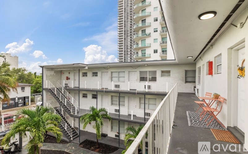 A balcony with chairs and a table is on the second floor of a white building.