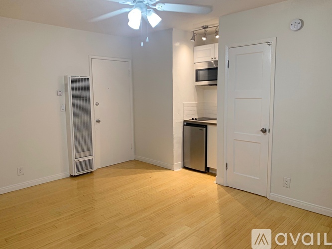 A room with a fan, a white door, and a kitchen area with a microwave and oven.