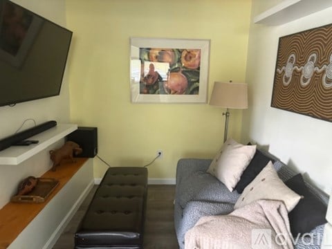A living room with a grey couch and a painting on the wall.