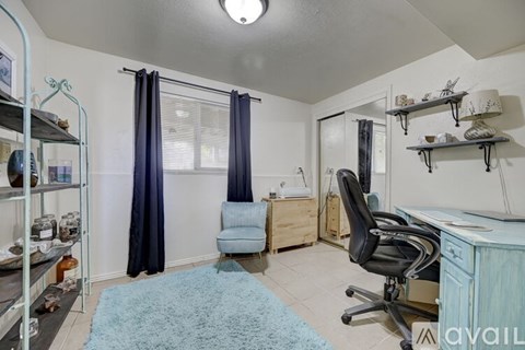 A room with a blue rug, a chair, and a desk with a computer.
