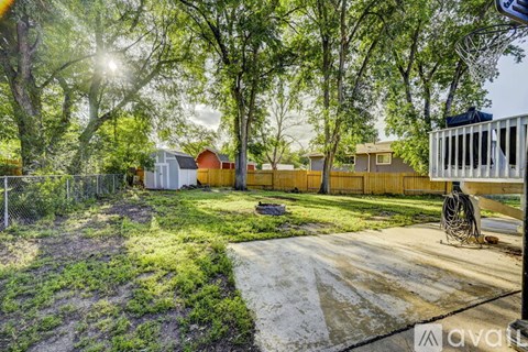 A backyard with a fence, a shed, and a basketball hoop.
