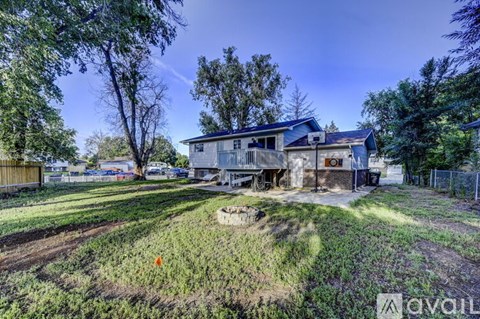 A house with a blue roof is surrounded by greenery and a dirt path.