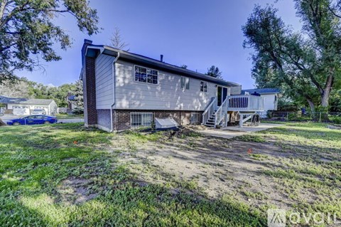 A house with a grey exterior and a white garage door is surrounded by greenery.