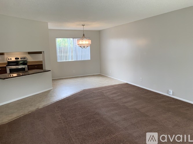 A spacious living room with a carpeted floor and a window with blinds.