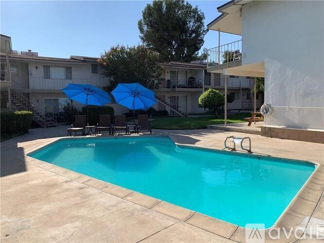 A swimming pool with blue umbrellas and a white building in the background.